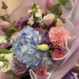 Pastel bouquet with blue hydrangea, pink roses, and purple blooms in pink wrap