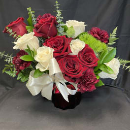 Red and white rose bouquet in a dark vase with a white ribbon