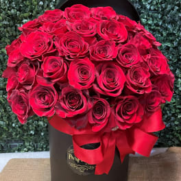 Red roses arranged in a black hat box with a red ribbon