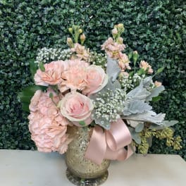 Pink roses and hydrangeas in a gold vase with a pink ribbon