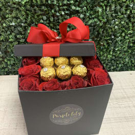 Black gift box with red roses and gold-wrapped chocolates topped by a red bow