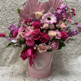 Pink and purple mixed flower arrangement in a pink hatbox with ribbon