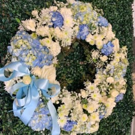 Heart-shaped floral wreath with blue and white flowers and a light blue ribbon
