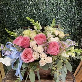 Pink and cream roses arranged in a wooden box with a blue ribbon