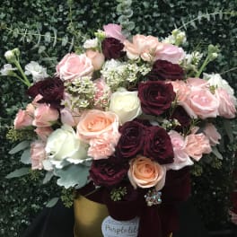 Bouquet of pink, burgundy, and white roses in a gold hatbox with ribbon