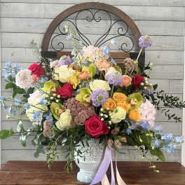 Colorful mixed flower arrangement in a white vase with ribbon tails