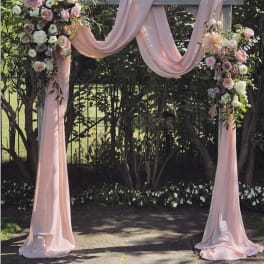 Pink draped wedding arch with pastel floral arrangements