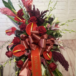 Red roses and tropical flowers arranged with a large ribbon bow