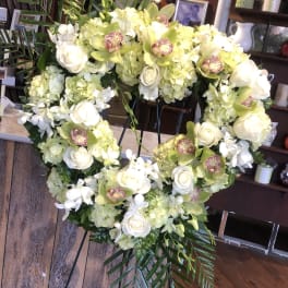 Heart-shaped floral wreath with white roses and pale green orchids on an easel