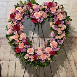 Heart-shaped floral wreath on a stand with pink, purple, and red blooms