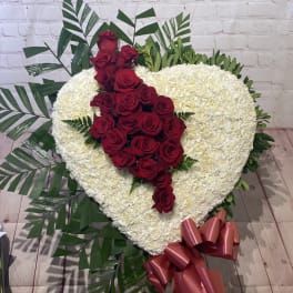 Heart-shaped white floral arrangement with red roses and a pink ribbon bow
