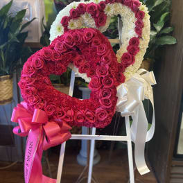 Two heart-shaped floral wreaths on a stand, one pink and one white with roses.