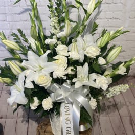 White lilies and roses arranged in a tall bouquet with a silver ribbon