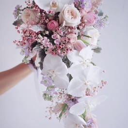 Cascade bouquet of white orchids, pale pink roses, and lavender flowers