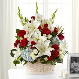 Basket arrangement of red roses, white lilies, and blue hydrangeas