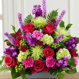 Mixed bouquet of pink roses, purple blooms, and green flowers in a rectangular vase
