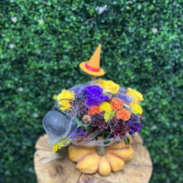 Colorful floral arrangement in a pumpkin-shaped container with a small witch hat