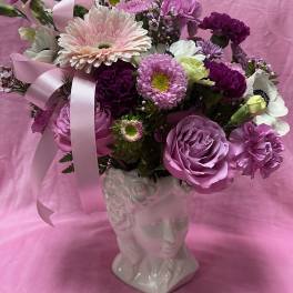 Pink and purple flower arrangement in a white face vase with ribbon