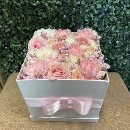 Pink and white roses arranged in a white box with a pink ribbon