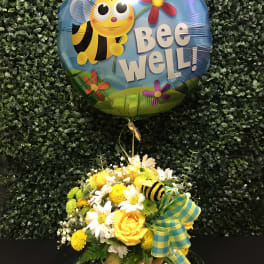 Bee Well balloon above a yellow and white flower arrangement in a vase