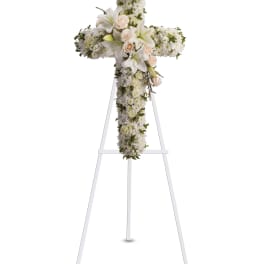 White floral cross on a white stand with lilies and roses