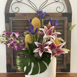 Tropical floral arrangement in a white vase with orchids and lilies