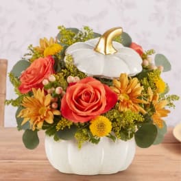 Pumpkin-shaped floral arrangement with orange roses and yellow daisies in a white container