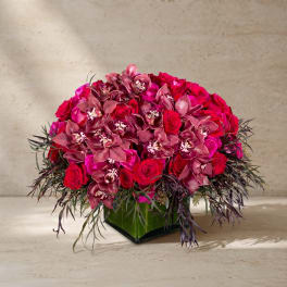 Pink roses and orchids arranged in a square glass vase