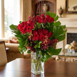 Red roses in a clear glass vase with burgundy accents