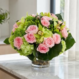 Pink roses and green orchids arranged in a clear glass vase