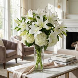 White lilies and hydrangeas arranged in a clear glass vase