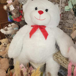Large white teddy bear with a red bow tie