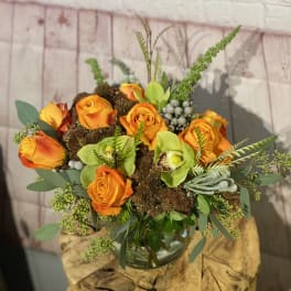 Orange roses and green orchids arranged in a glass vase