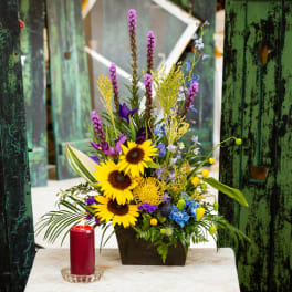 Sunflower arrangement in a dark container with a red candle beside it
