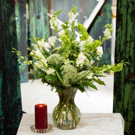 White and green floral arrangement in a glass vase beside a red candle.