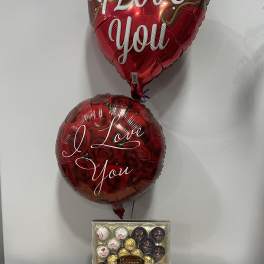 Two heart-shaped balloons with love messages above a box of Ferrero chocolates