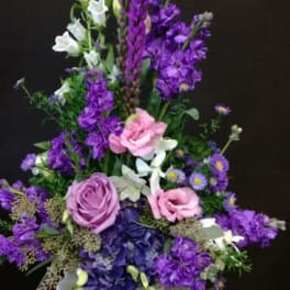 Tall purple and pink floral arrangement in a white pedestal vase