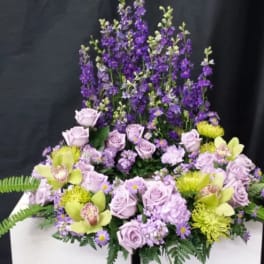 Lavender roses and purple flowers arranged in a tall display with green accents.