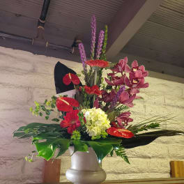 Tall mixed floral arrangement in a white vase with red and purple blooms