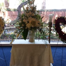 Heart-shaped floral wreaths on stands flank a white vase arrangement on a table.