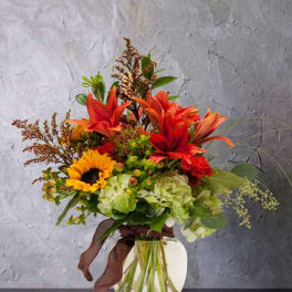 Bouquet of red lilies, sunflowers, and green hydrangeas in a glass vase