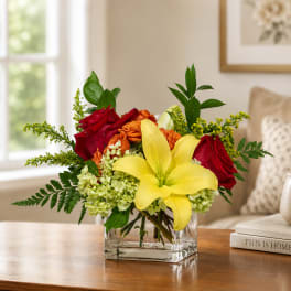 Bouquet of red roses and a yellow lily in a clear square vase