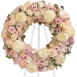 Round floral wreath of pale pink and cream roses on a white stand