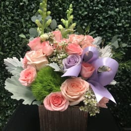 Pink and lavender roses in a square wooden box with a purple ribbon