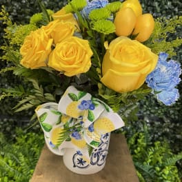 Yellow roses and blue carnations in a patterned mug with a bow