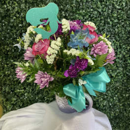 Mixed pink and purple bouquet in a white mug with a teal ribbon