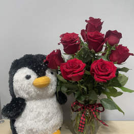 Red roses in a glass vase beside a plush penguin