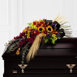 Colorful floral casket spray with sunflowers and lilies on a dark casket