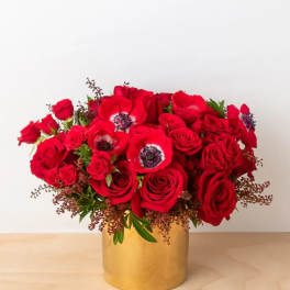 Red roses and red anemones arranged in a gold vase