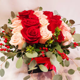 Red and blush roses arranged in a black box with eucalyptus and red berries